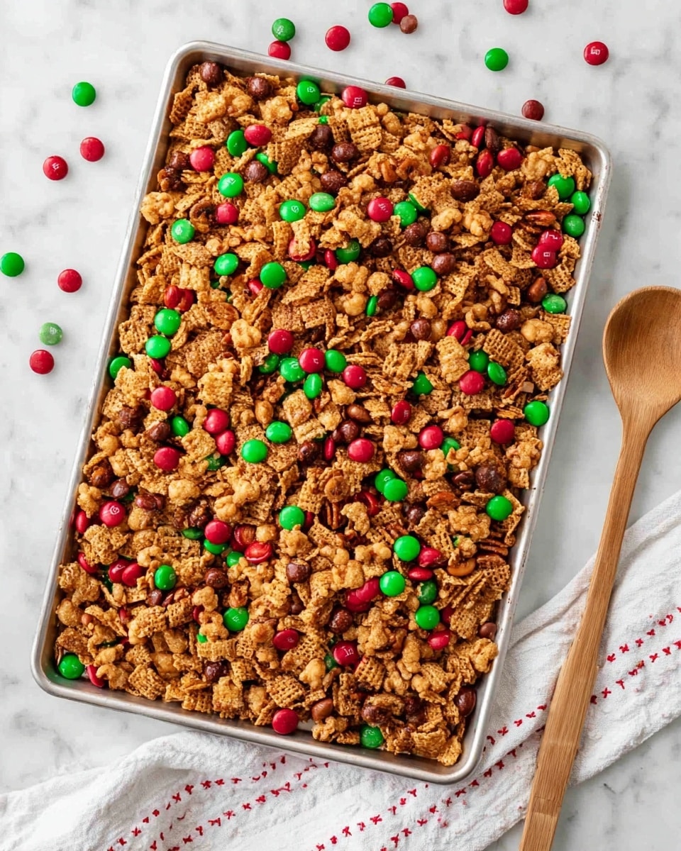 A large silver baking tray is filled with a mix of golden brown crunchy cereal pieces and nuts, scattered with small round candy-coated chocolates in bright red and green colors. The mix looks crispy and textured, with the candies sitting on top and a few scattered outside the tray on a white marbled surface. A wooden spoon with a smooth light brown finish rests on the bottom right corner of the tray, and a white cloth with red stitched lines lies nearby. The overall scene is bright and festive, with a top-down view capturing all the details clearly. photo taken with an iphone --ar 4:5 --v 7