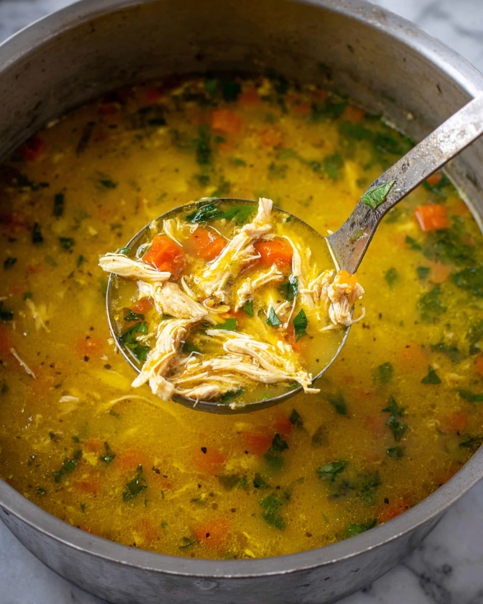 The image shows a close-up of a silver pot filled with thick yellow soup that has shredded chicken pieces, small orange carrot cubes, and green leafy herbs floating in it. A metal ladle with soup and chicken is lifted above the pot, showing the texture of the shredded chicken and diced carrots in the yellow broth. The pot sits on a surface with a white marbled texture. photo taken with an iphone --ar 4:5 --v 7