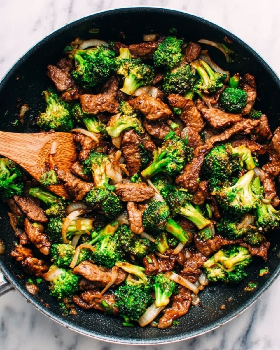 The image shows a black pan filled with cooked beef strips and bright green broccoli florets mixed together. The beef pieces are brown and slightly crispy, while the broccoli looks fresh and tender. There is a wooden spatula partially visible, stirring or scooping the food. The colors are warm and natural, with the dark brown of the beef contrasting the vivid green of the broccoli. The pan sits on a white marbled surface. Photo taken with an iphone --ar 4:5 --v 7