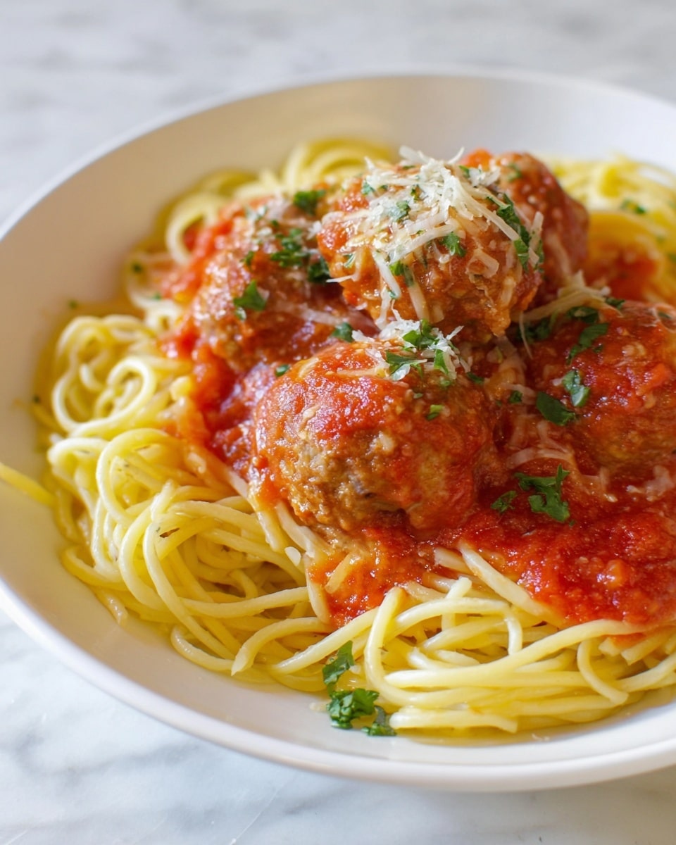 A white plate holds a serving of long, yellow spaghetti noodles arranged in a loose nest at the base. On top of the spaghetti are three large, round meatballs coated in bright red tomato sauce with a slightly chunky texture. The sauce spreads unevenly over the meatballs and noodles, with some bits of chopped green herbs sprinkled on top. Shredded pale yellow cheese melts slightly over one meatball, adding a creamy texture. The plate is set on a white marbled surface. photo taken with an iphone --ar 4:5 --v 7