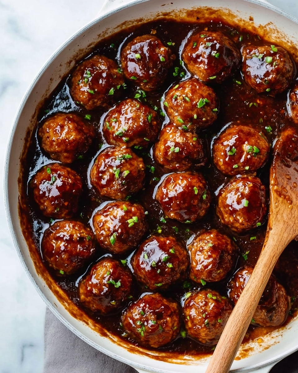 A white pan filled with round, shiny meatballs covered in a thick, dark brown sauce. The meatballs are arranged closely together, showing a cooked, caramelized texture with small green herb bits sprinkled on top. A wooden spoon is partially inside the pan on the right side. The pan is placed on a white marbled surface. Photo taken with an iphone --ar 4:5 --v 7