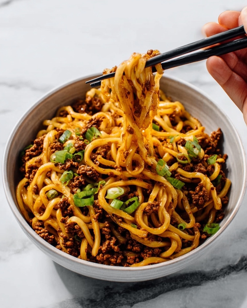 A white bowl filled with thick noodles mixed with small pieces of brown cooked meat and garnished with light green chopped scallions. A pair of black chopsticks held by a woman's hand lifts some noodles mid-air showing the noodles' soft and slightly oily texture with bits of meat clinging to them. The background and surface are white marbled texture. photo taken with an iphone --ar 4:5 --v 7