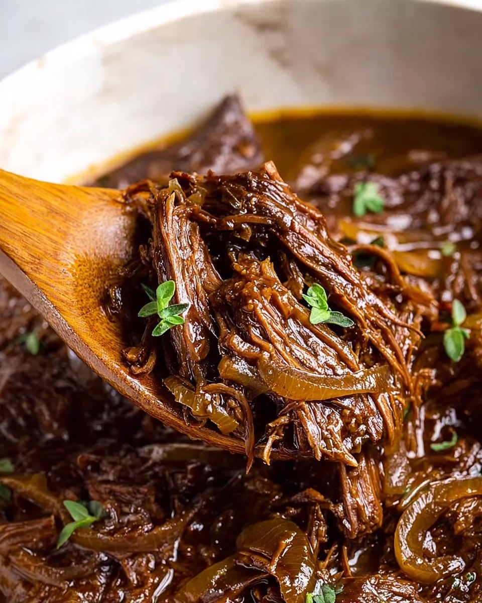 A close-up view of a rich, dark brown shredded beef stew with visible strands of tender meat soaked in a thick, glossy sauce. Thin slices of caramelized onions are mixed throughout, adding texture and depth. Small fresh green herb leaves are scattered on the beef, providing a touch of color contrast. The dish is shown in a white marbled bowl, with a wooden spoon lifting a portion of the stew, highlighting the moist, fibrous texture of the meat. The background is a white marbled surface. Photo taken with an iphone --ar 4:5 --v 7