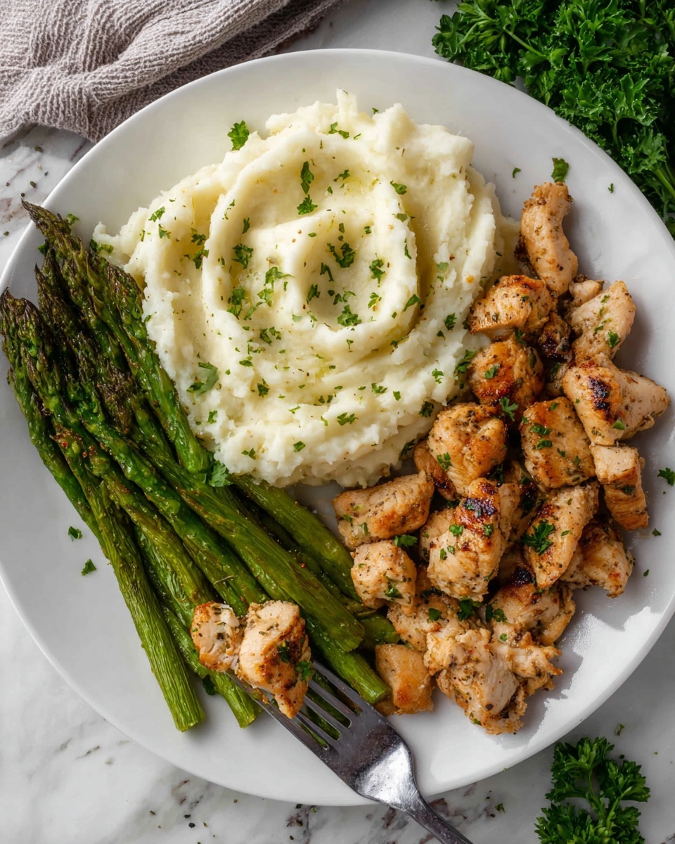 The white plate shows a meal with three parts arranged side by side: on the left, a small bunch of bright green grilled asparagus spears with a slight char, in the middle, a big scoop of creamy, light off-white mashed potatoes with a small swirl pattern on top and some green herbs sprinkled, and on the right, several pieces of golden-brown cooked chicken pieces with a slight crispy texture and some green herb bits on top; a silver fork holds one asparagus spear near the bottom, and some fresh green parsley is seen near the top right next to the plate, all set on a white marbled surface photo taken with an iphone --ar 4:5 --v 7
