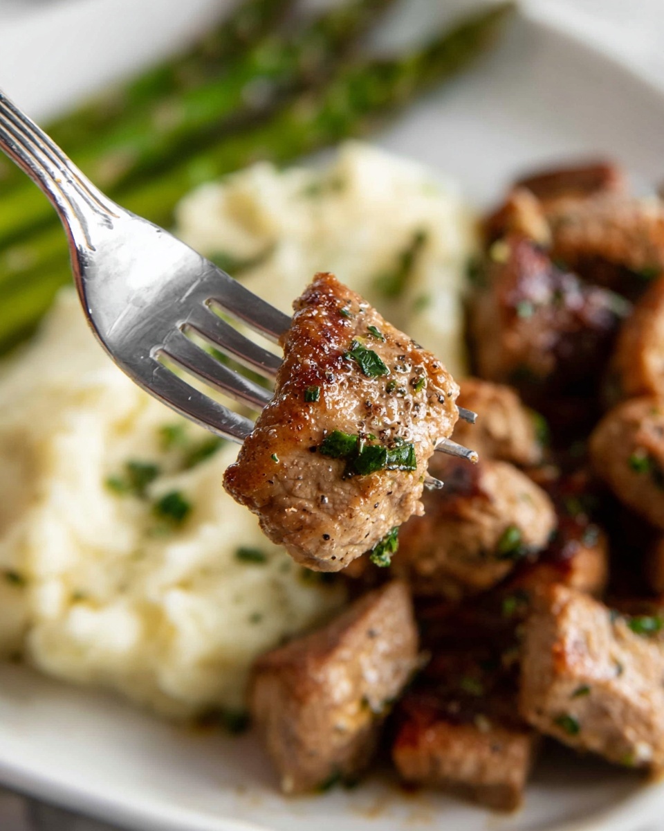 The image shows a close-up of a piece of cooked meat held by a fork, which is lightly browned with a slightly crispy texture and sprinkled with green herbs and black pepper. The meat piece is in the foreground with a bunch of similar browned meat pieces spread across a white plate below. Behind the meat, there is a soft, creamy layer of mashed potatoes with a light sprinkling of green herbs for garnish. On the left side of the plate, tender green asparagus spears add a fresh, vibrant layer. The whole scene is set on a white marbled surface. Photo taken with an iphone --ar 4:5 --v 7