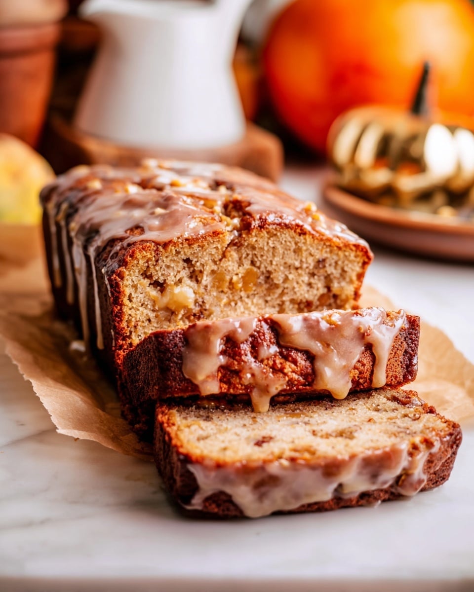 A loaf of cake with three sliced pieces in front shows a soft, light brown inside with visible bits of fruit or nuts. The top layer is darker brown with a shiny glaze that drips down the sides, giving it a moist look. The cake sits on a piece of parchment paper on a white marbled surface. The background has blurred objects like a small white pitcher, an orange pumpkin, and wooden and golden items that add warm autumn colors. The photo is close-up and bright, focusing on the texture of the cake. photo taken with an iphone --ar 4:5 --v 7