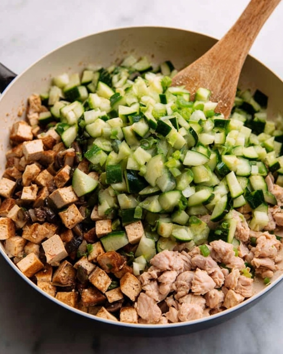 The image shows a close-up of a white pan filled with chopped ingredients being stirred by a woman’s hand holding a wooden spoon. The pan contains three layers of food: the bottom layer has small cubes of brown cooked tofu with a firm texture, the middle layer is diced light pink chicken pieces, and the top layer has bright green chopped cucumber with a fresh, smooth surface. The background is a white marbled texture. Photo taken with an iphone --ar 4:5 --v 7
