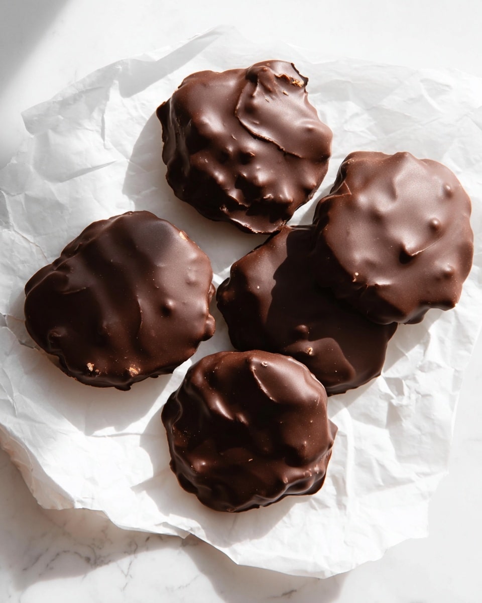 Five round, irregularly shaped treats coated in smooth dark brown chocolate sit on crinkled white paper over a white marbled surface. Each piece shows slight bumps and uneven textures under the chocolate layer, suggesting a crunchy filling inside. The chocolate coating is thick and glossy with some small raised areas and ridges. The arrangement is casual, with some pieces closer together and others slightly apart, all casting soft shadows on the white paper beneath them. The image has bright, natural lighting to highlight the rich chocolate color and the soft folds of the paper. photo taken with an iphone --ar 4:5 --v 7