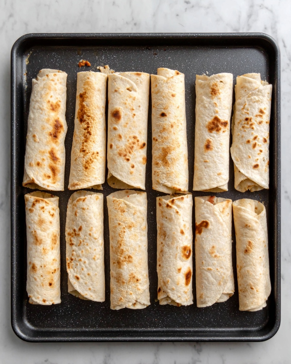 The image shows eight rolled flatbreads or tortillas placed in a single row on a black baking tray. Each roll is light brown with some darker toasted spots, and the edges are slightly uneven, showing a soft but cooked texture. The tray is clean except for a few small crumbs or tiny bits near the rolls. The background is a white marbled surface. The photo taken with an iphone --ar 4:5 --v 7
