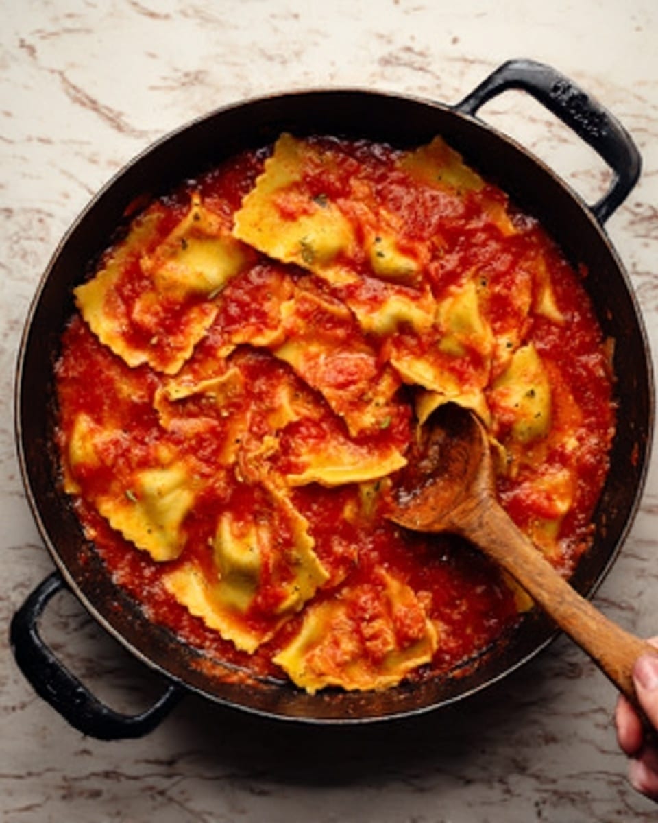 The image shows a black pan with two handles, filled with a rich red sauce mixed with pieces of yellow pasta. The pasta pieces are large and flat, some submerged in the sauce while others float on top, showing smooth, slightly folded edges. A wooden spoon rests inside the pan on the right side, with a woman's hand holding it gently. The background surface is a white marbled texture. The colors are warm and inviting, with the red sauce and yellow pasta providing a nice contrast. Photo taken with an iphone --ar 4:5 --v 7