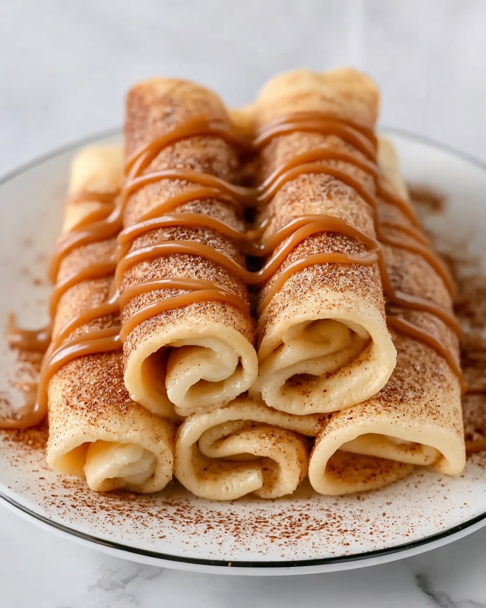 The image shows five light golden brown rolled crepes stacked in two layers on a white plate with a thin black rim, arranged in a pyramid shape with three crepes at the bottom and two on top. The crepes have a slightly soft texture and are sprinkled with a layer of cinnamon powder giving a light brown dusted look. Over the top crepes, there are thick lines of caramel sauce drizzled in a wavy pattern from left to right down the stack, adding a smooth and shiny texture contrast. The background and surface are a white marbled texture, and the photo is taken with an iphone --ar 4:5 --v 7