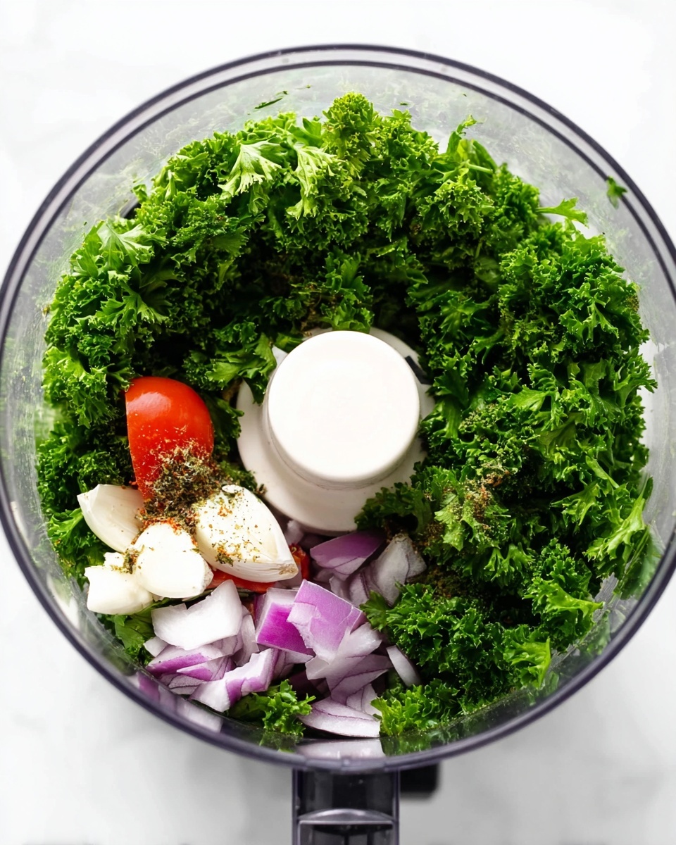 A clear food processor bowl filled with dense, bright green curly parsley leaves layered mostly on the bottom and sides. On top of the parsley, there are a few pieces of purple onion chunks, small white cloves of garlic, and small chunks of red tomato. Some small brownish herbs or spices are sprinkled over the onion and garlic. The bowl sits on a white marbled surface with the white food processor blade holder visible in the center. photo taken with an iphone --ar 4:5 --v 7