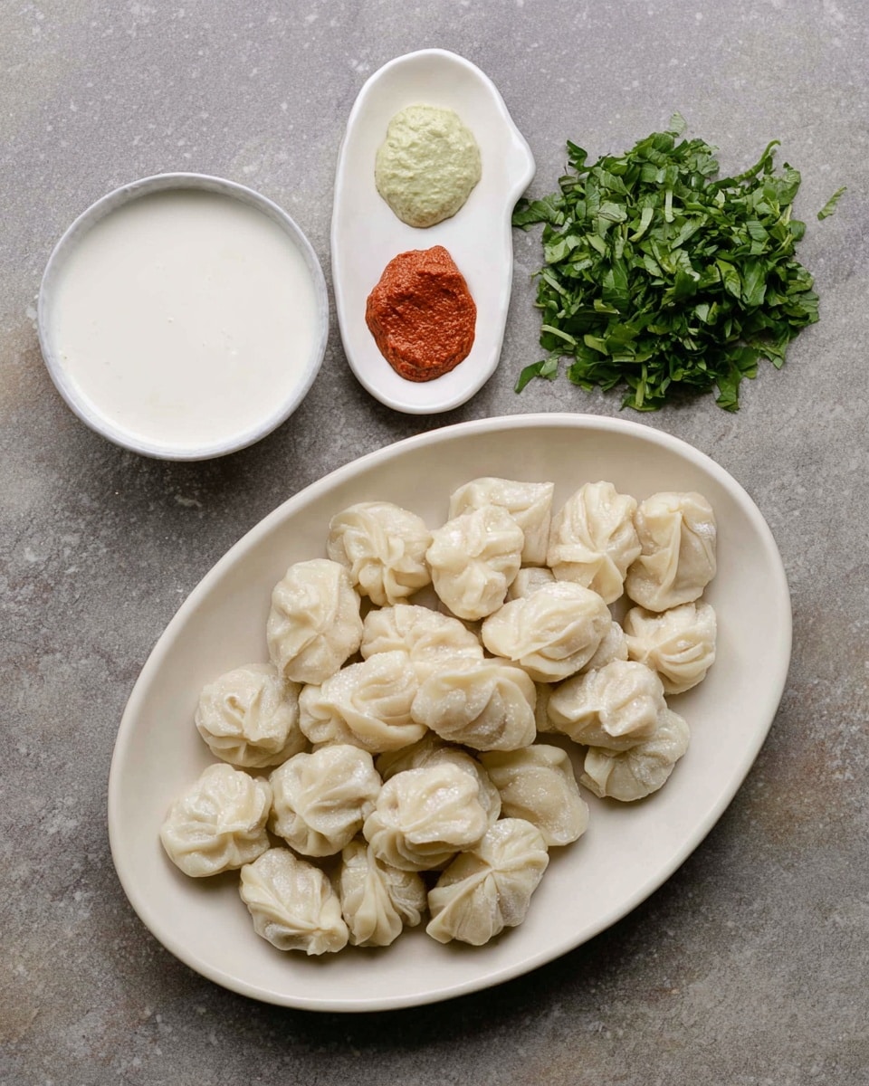 The image shows a white oval plate filled with many small, white dumplings that have a soft, slightly wrinkled skin and are arranged in a neat pile. To the right of the plate, there is a small pile of finely chopped green leafy herbs. Above the dumplings, there is a white round bowl filled with a smooth white liquid, possibly a dipping sauce. To the left of the bowl, a white irregularly shaped small dish holds four small dollops of different pastes: one large reddish-brown, one light brown, one pale green, and one creamy white. All the items are placed on a white marbled surface. Photo taken with an iphone --ar 4:5 --v 7