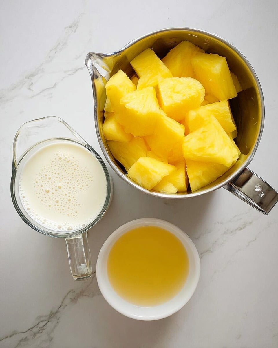 A white metal measuring cup filled with bright yellow pineapple chunks sits on the left side, next to a clear glass measuring cup filled with a creamy white liquid with small bubbles on top, placed on the right side; below them is a small white round dish holding a smooth golden-yellow liquid, all set on a white marbled surface photo taken with an iphone --ar 4:5 --v 7