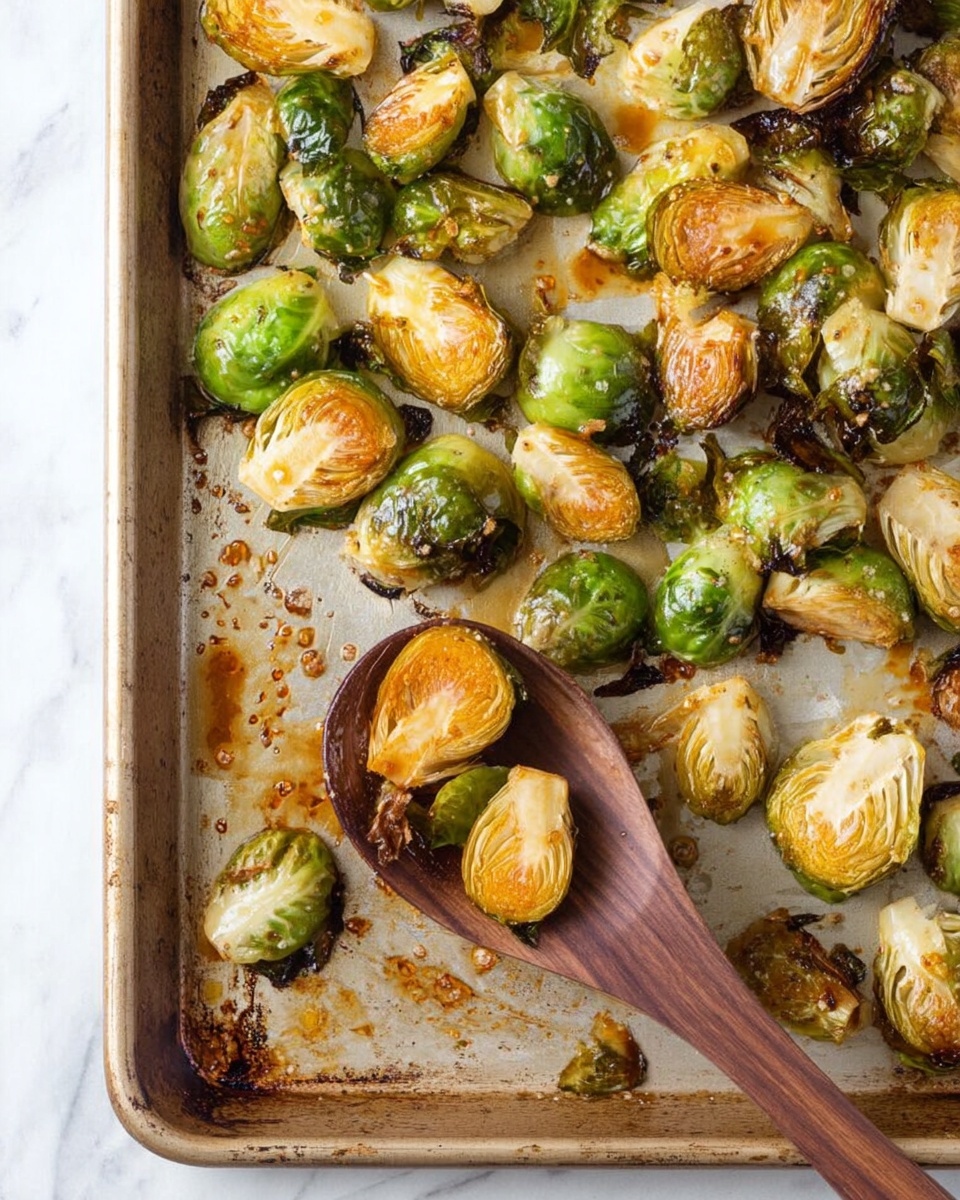 A baking tray filled with roasted Brussels sprouts, cut in half showing layers of green and light brown with some crispy, darker brown edges. The sprouts have a slightly shiny, roasted texture with some caramelized spots. A wooden spoon rests on the tray, holding two halved sprouts. The tray is placed on a white marbled surface, showing bits of browned seasoning and oil stains around the sprouts. photo taken with an iphone --ar 4:5 --v 7