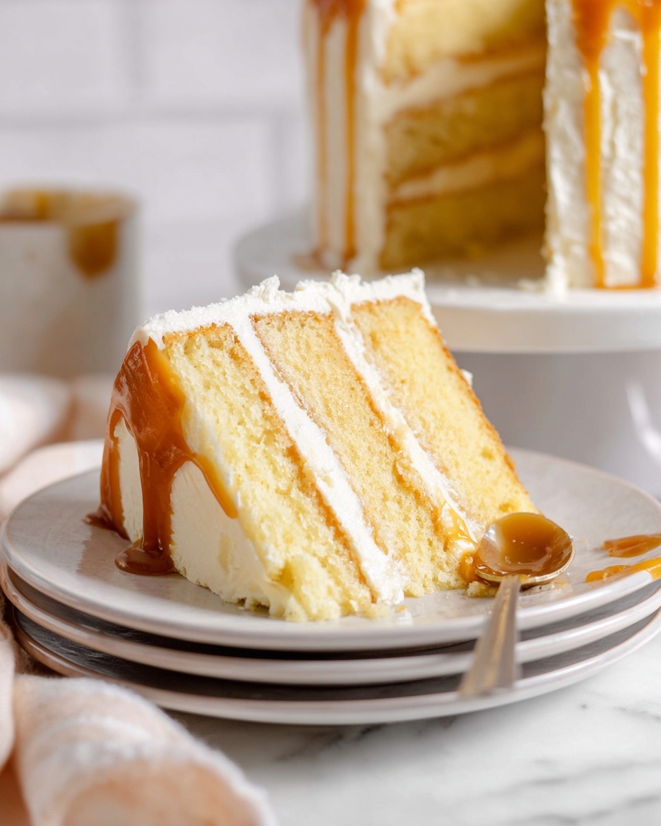 A slice of three-layer yellow cake sits on two stacked white plates, each cake layer soft and light yellow. Between the layers are two lines of smooth caramel sauce and white creamy frosting. The outside edges of the cake slice are coated with a thick layer of white frosting and caramel sauce that drips slightly onto the plates. The background shows a soft focus of the whole cake, and a spoon with caramel sauce rests on the white marbled surface near the plates. Photo taken with an iphone --ar 4:5 --v 7