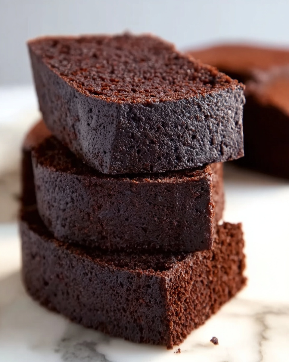 The image shows three thick slices of dark chocolate cake stacked on top of each other on a white marbled surface, with a fourth slice blurred in the background. The cake has a moist and slightly rough texture with a deep brown color. The edges of the slices are sharp and even, showing a dense but soft crumb inside. The overall look is rich and inviting. photo taken with an iphone --ar 4:5 --v 7