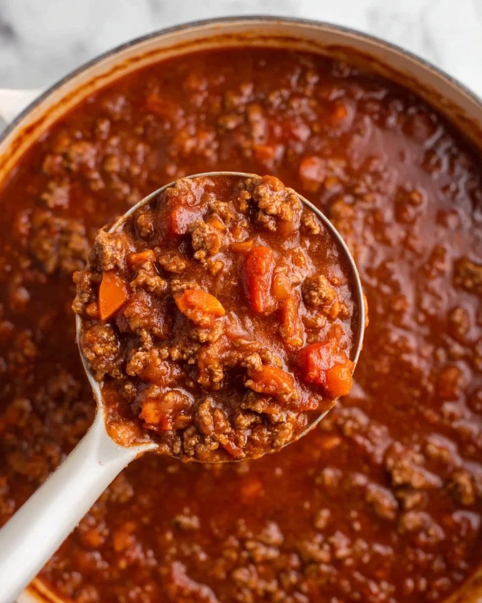 A close-up view shows a white ladle filled with thick, hearty chili containing ground meat, chunks of tomatoes, and slices of carrots in a rich, dark red sauce. The ladle is held over a large pot filled with the same chunky chili mixture, resting against a white marbled surface. The textures in the chili are dense with visible small pieces of vegetables and meat clearly blending into the thick sauce. photo taken with an iphone --ar 4:5 --v 7