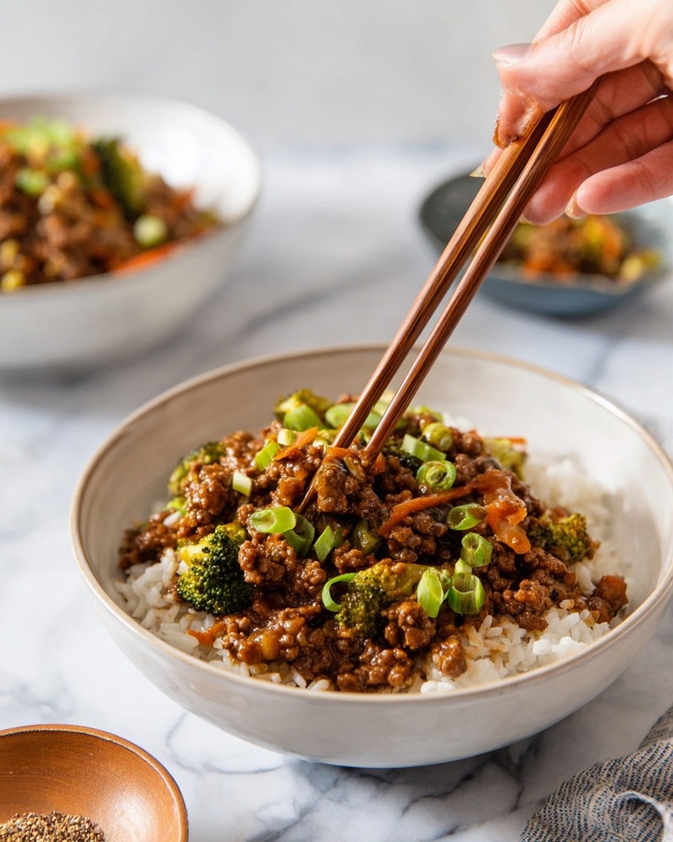 A white bowl filled with a base layer of white rice, topped with a mixed layer of cooked ground meat and vegetables like small broccoli pieces, carrot strips, and chopped green onions, all coated in a glossy brown sauce. A woman's hand holding wooden chopsticks reaches into the bowl, picking up some of the food. In the background, there is another white bowl with a similar dish, and a small brown bowl with a seasoning on a white marbled surface. The photo taken with an iphone --ar 4:5 --v 7