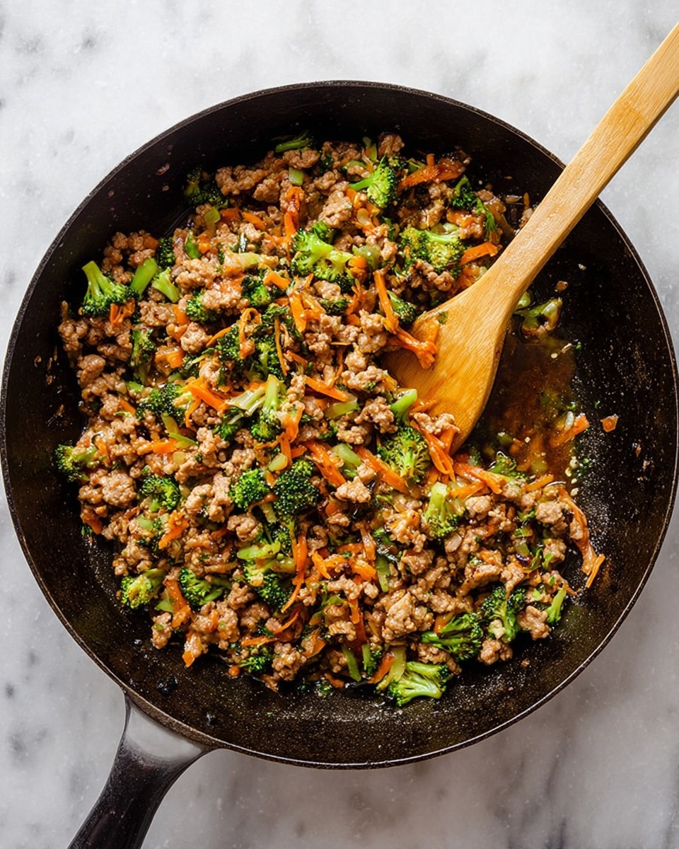 A black cast iron pan filled with cooked minced meat mixed with small pieces of bright green broccoli and shredded orange carrots, all sitting in a brown sauce that glistens slightly. A wooden spatula rests inside the pan, partially stirring the mixture, showing the textures of the tender meat and crisp vegetables. The pan is placed on a white marbled surface. photo taken with an iphone --ar 4:5 --v 7