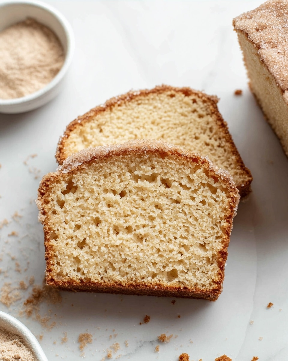 The image shows two slices of soft, light brown cake placed one on top of the other on a white marbled surface. The cake has a moist and airy texture with small holes visible throughout the slice. The top of the slice has a crumbly, darker brown crust with a sugar coating, giving a slightly rough texture. Crumbs are scattered around the slices on the surface. Part of a white bowl with a light brown powder mix is visible to the left side of the image. photo taken with an iphone --ar 4:5 --v 7