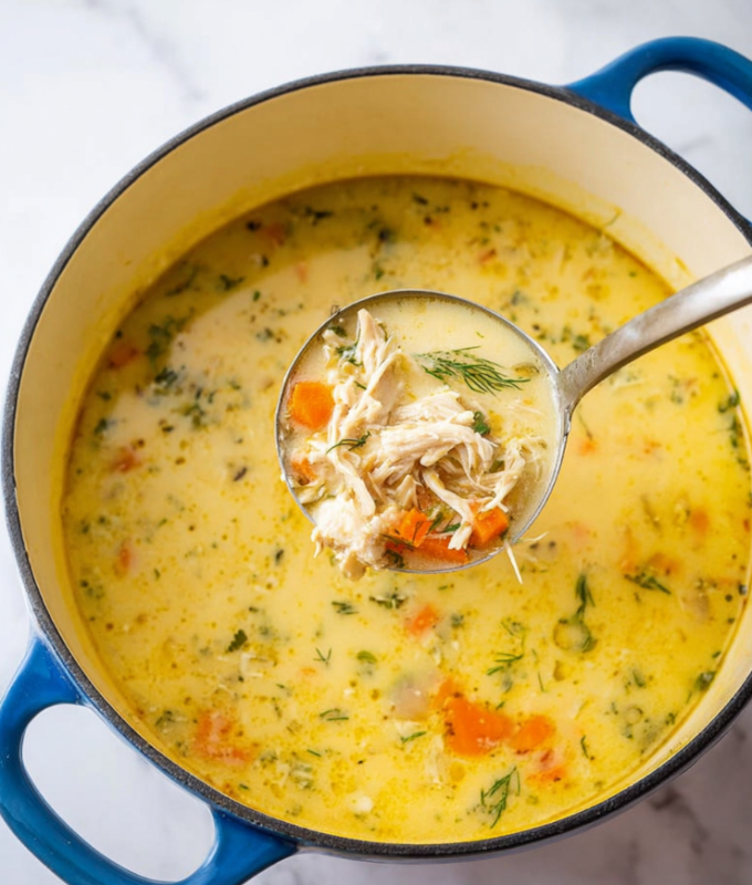 The image shows a white pot with blue handles filled with thick creamy yellow soup. Inside the soup, there are pieces of shredded light beige chicken and small orange carrot chunks. There are small green dill leaves floating on the surface, adding a fresh touch. A silver ladle is scooping a portion of the soup, holding chicken, carrots, and some broth. The pot sits on a white marbled surface. The photo taken with an iphone --ar 4:5 --v 7