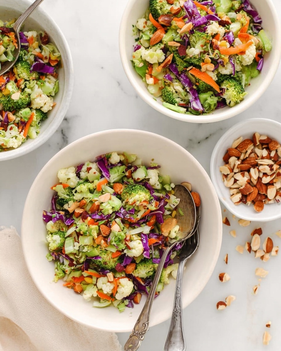 The image shows three white bowls on a white marbled surface. Each bowl is filled with a colorful salad made of small pieces of green broccoli, orange carrot slivers, purple cabbage, light green celery, white cauliflower, and chopped brown almonds. Two old silver forks rest inside two of the bowls. To the right, there is a small white bowl filled with more chopped almonds, some scattered nearby. A woman's hand is holding one of the bowls in the top left corner. Photo taken with an iphone --ar 4:5 --v 7