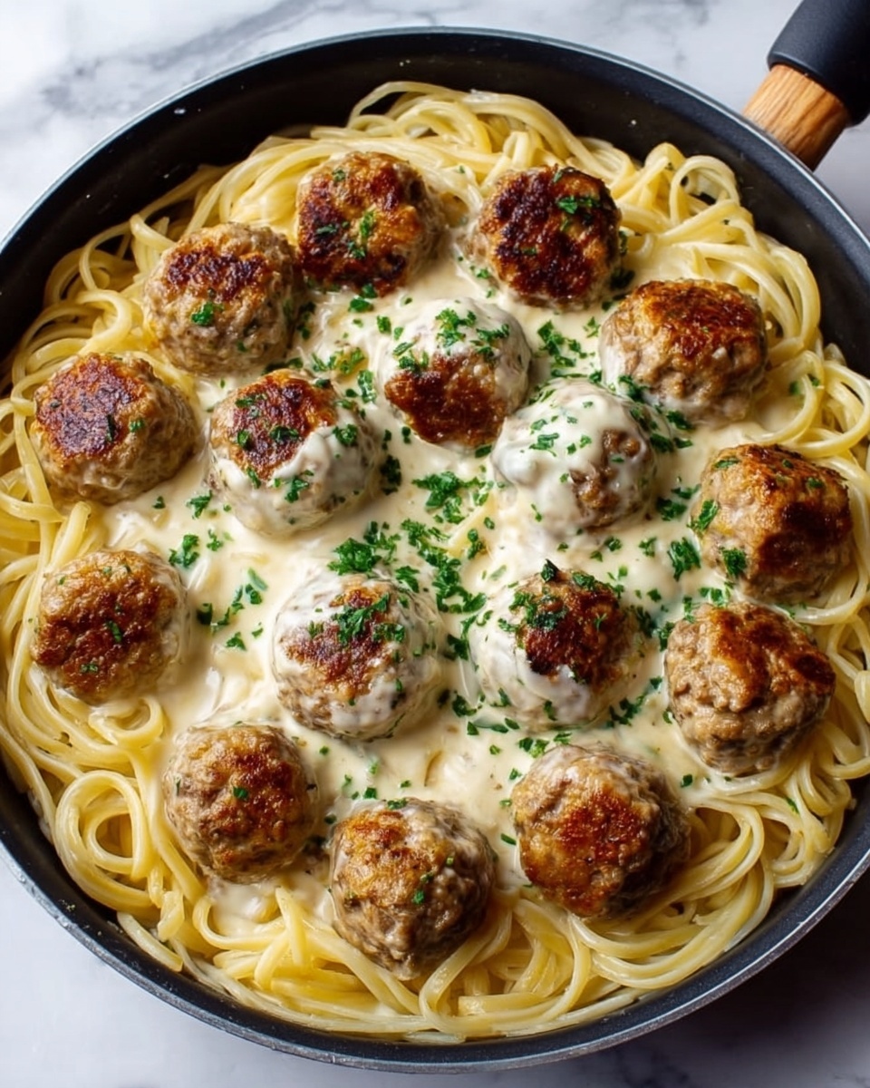 The image shows a black pan filled with long spaghetti noodles spread evenly in the bottom layer. On top of the noodles is a creamy white sauce, smooth and thick. Sitting above the sauce are about twelve browned meatballs, each with a slightly crispy texture and sprinkled with chopped green herbs. The pan is placed on a white marbled surface. Photo taken with an iphone --ar 4:5 --v 7