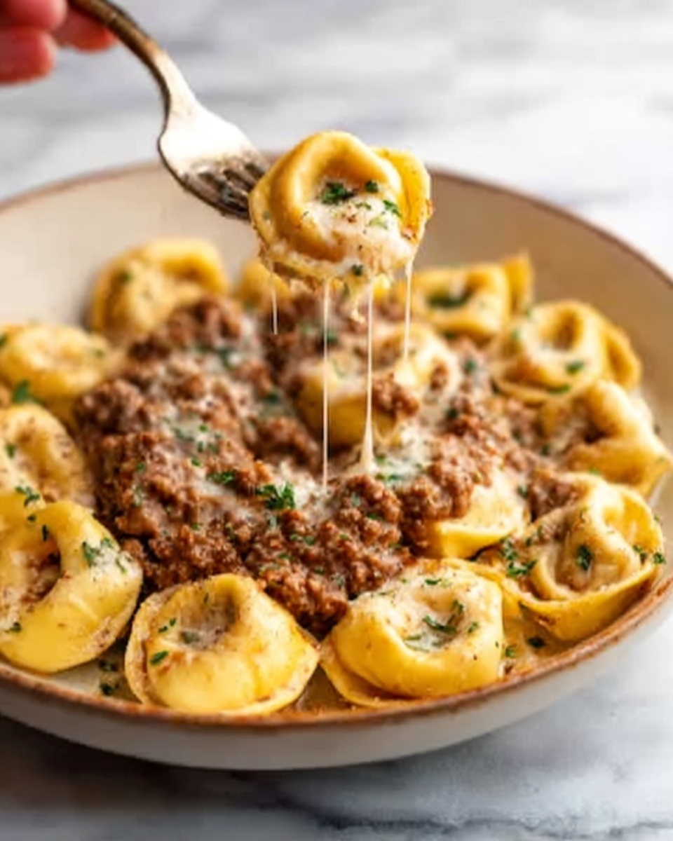 The image shows a close-up of a creamy pasta dish with round, stuffed tortellini arranged in a single layer, golden yellow in color with soft folds visible. On top, there is a thick layer of ground meat sauce, brown and textured with small bits of herbs sprinkled evenly over it. A woman's hand is holding a fork lifting one piece of tortellini, with melted cheese stretching from the fork back to the plate. The dish is in a white bowl on a white marbled surface. photo taken with an iphone --ar 4:5 --v 7