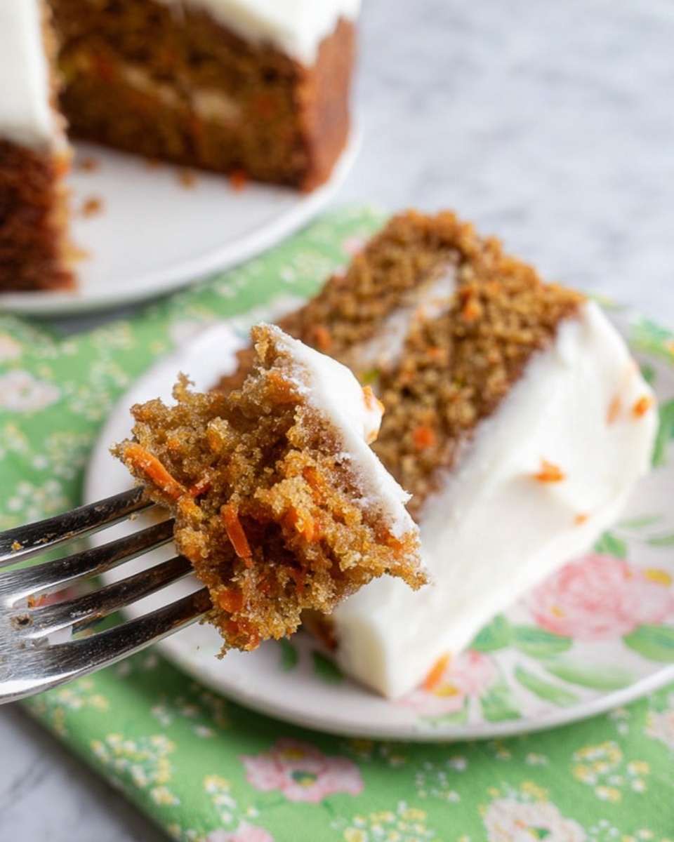 A close-up of a moist carrot cake slice held by a fork, showing one layer of soft, textured cake with shredded orange carrot pieces inside. The cake has a light brown color with small nut bits throughout. The top of the cake layer is covered with a smooth white frosting, slightly thick, and a small amount of frosting clings to the fork. In the background, a larger piece of the same carrot cake is on a white plate with a green floral cloth beneath it, and the scene is set on a white marbled surface. photo taken with an iphone --ar 4:5 --v 7