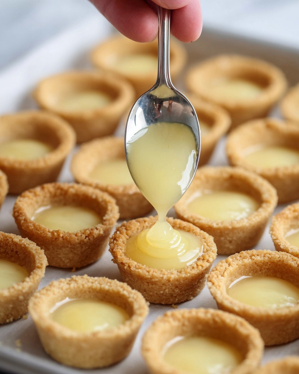 The image shows small tart shells arranged on a tray with a white marbled surface in the background. Each shell is golden brown with a crumbly texture and hollow center, and some are filled with a smooth, pale yellow filling that looks glossy. A silver spoon is held by a woman's hand, pouring the pale yellow filling into one of the tart shells, with the filling gently flowing into the shell, creating a shiny, smooth surface inside. The focus is on the spoon and the tart shells in the front, while more tart shells are blurred in the background. Photo taken with an iphone --ar 4:5 --v 7