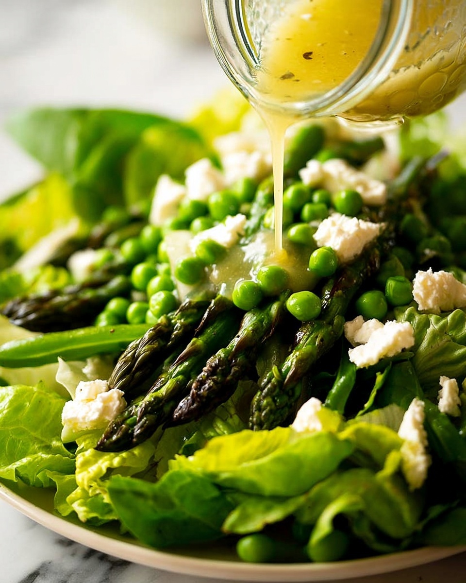 A fresh salad is shown with three layers: the bottom layer is bright green lettuce leaves, the middle layer has cooked asparagus spears that are dark green and slightly shiny, and the top layer contains bright green peas and small white chunks of soft cheese scattered on top. A clear glass jar is held above the salad, pouring a light yellow dressing over the vegetables. The salad sits on a white plate with a white marbled surface in the background. Photo taken with an iphone --ar 4:5 --v 7