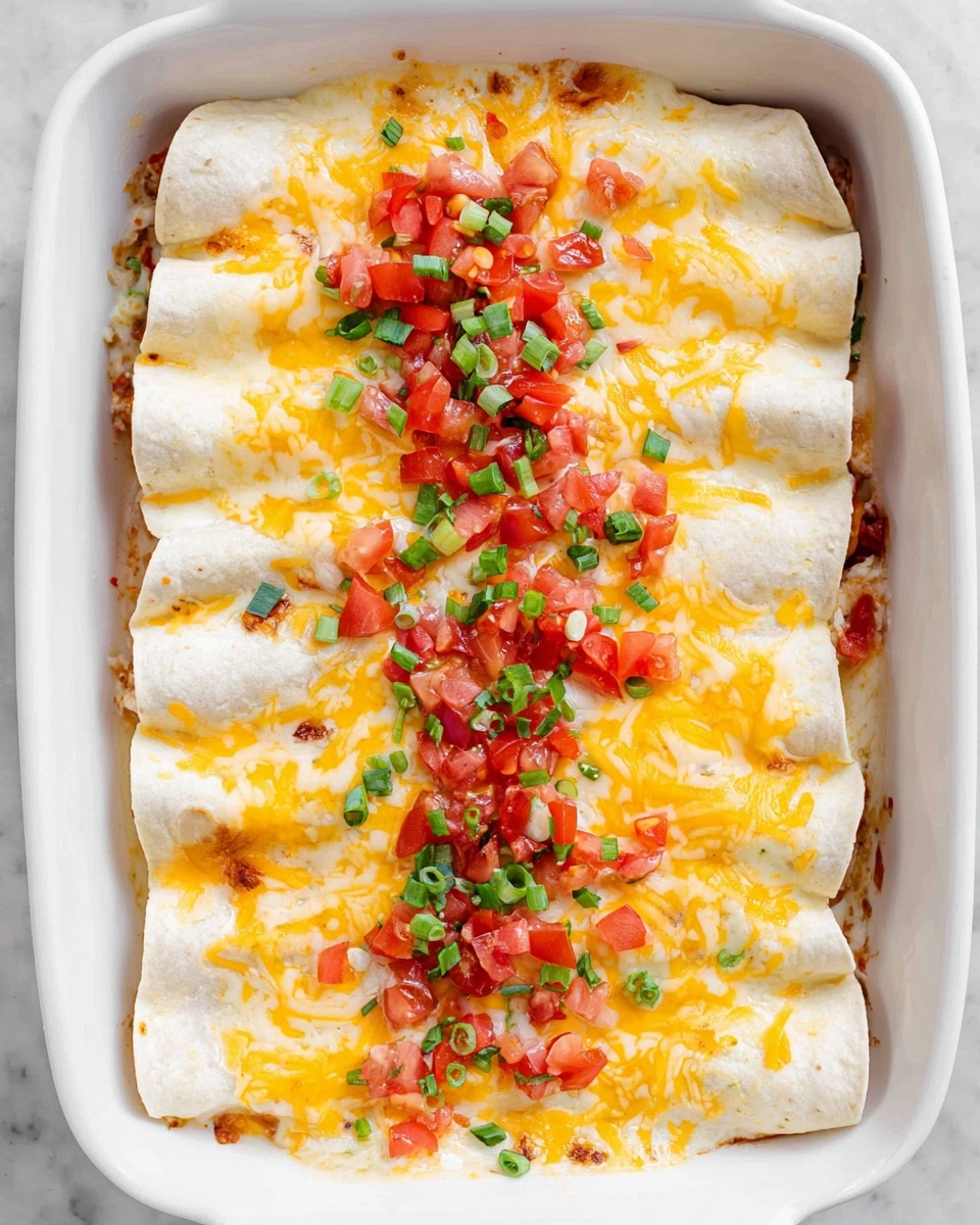 There is a white dish filled with two layers of rolled tortillas lying side by side, about eight in total. The top layer is covered with melted yellow and white cheese, scattered in an uneven pattern, with diced red tomatoes and green chopped onions spread across the surface. The tortillas underneath are white and soft, and you can see bits of filling peeking out slightly. The background is a white marbled surface. photo taken with an iphone --ar 4:5 --v 7