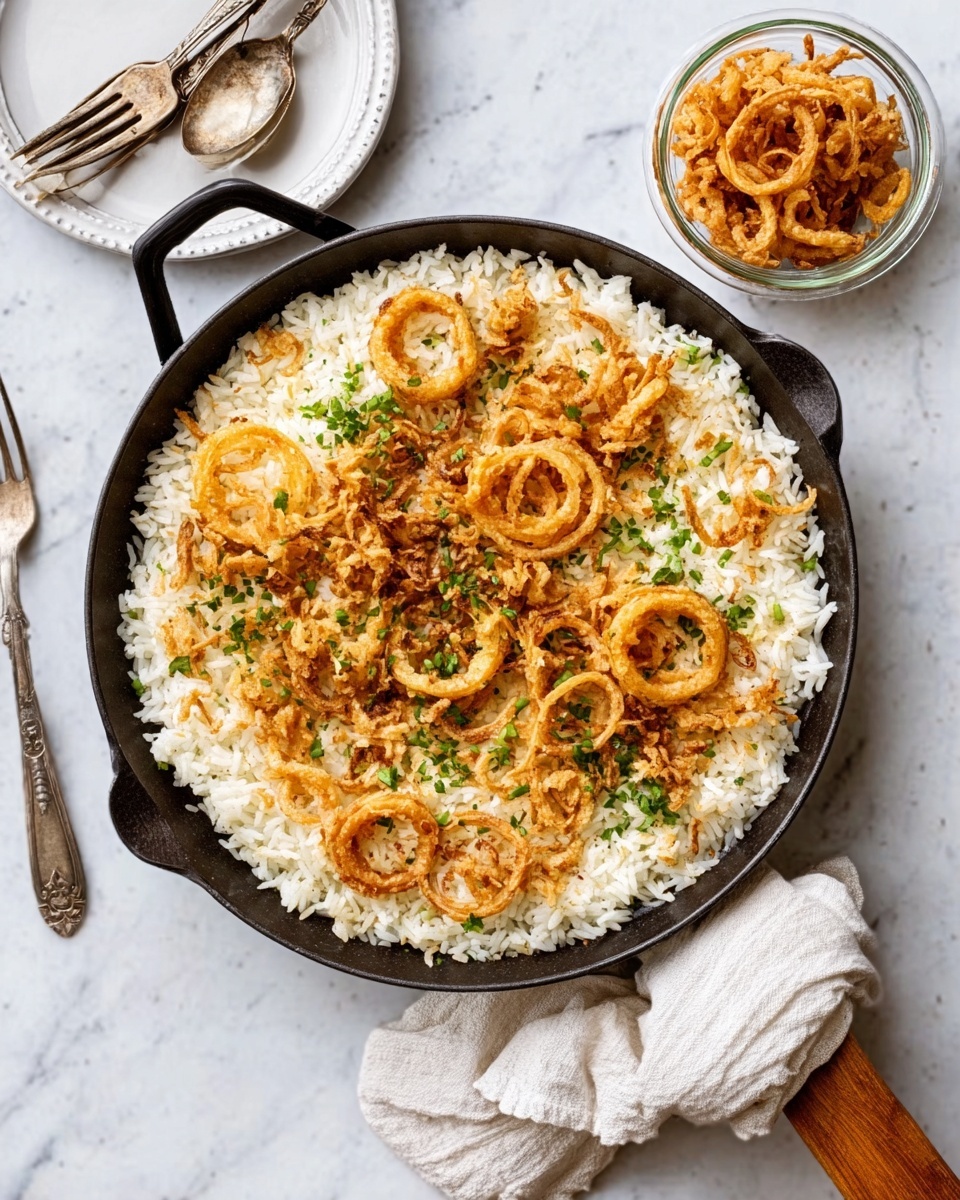 A black pan filled with a round layer of creamy white rice, topped with light golden crispy fried onion rings scattered unevenly across the top. Small green herb pieces are spread gently over the rice, adding a touch of color. The pan sits on a white marbled surface, next to a small glass bowl filled with more fried onion rings. Nearby is a round white plate holding two silver forks and knives. A wooden spoon with a white cloth partially covers the pan handle. Photo taken with an iphone --ar 4:5 --v 7