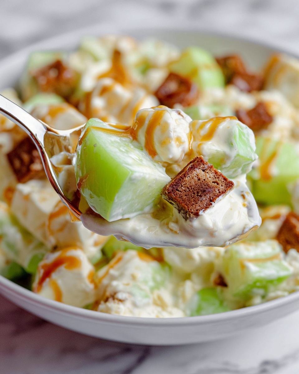 This image shows a close-up of a spoonful of a creamy fruit salad. The spoon holds three main parts: green apple pieces that are light green with a smooth texture, white creamy mixture that looks thick and soft, and small brown cake-like cubes with a dense texture. The fruit salad is in a white bowl filled with the same mix, displaying green apple chunks, white cream, and brown cake cubes scattered evenly. Some caramel sauce is drizzled lightly on top, adding a glossy amber color. The background is a white marbled surface. Photo taken with an iphone --ar 4:5 --v 7