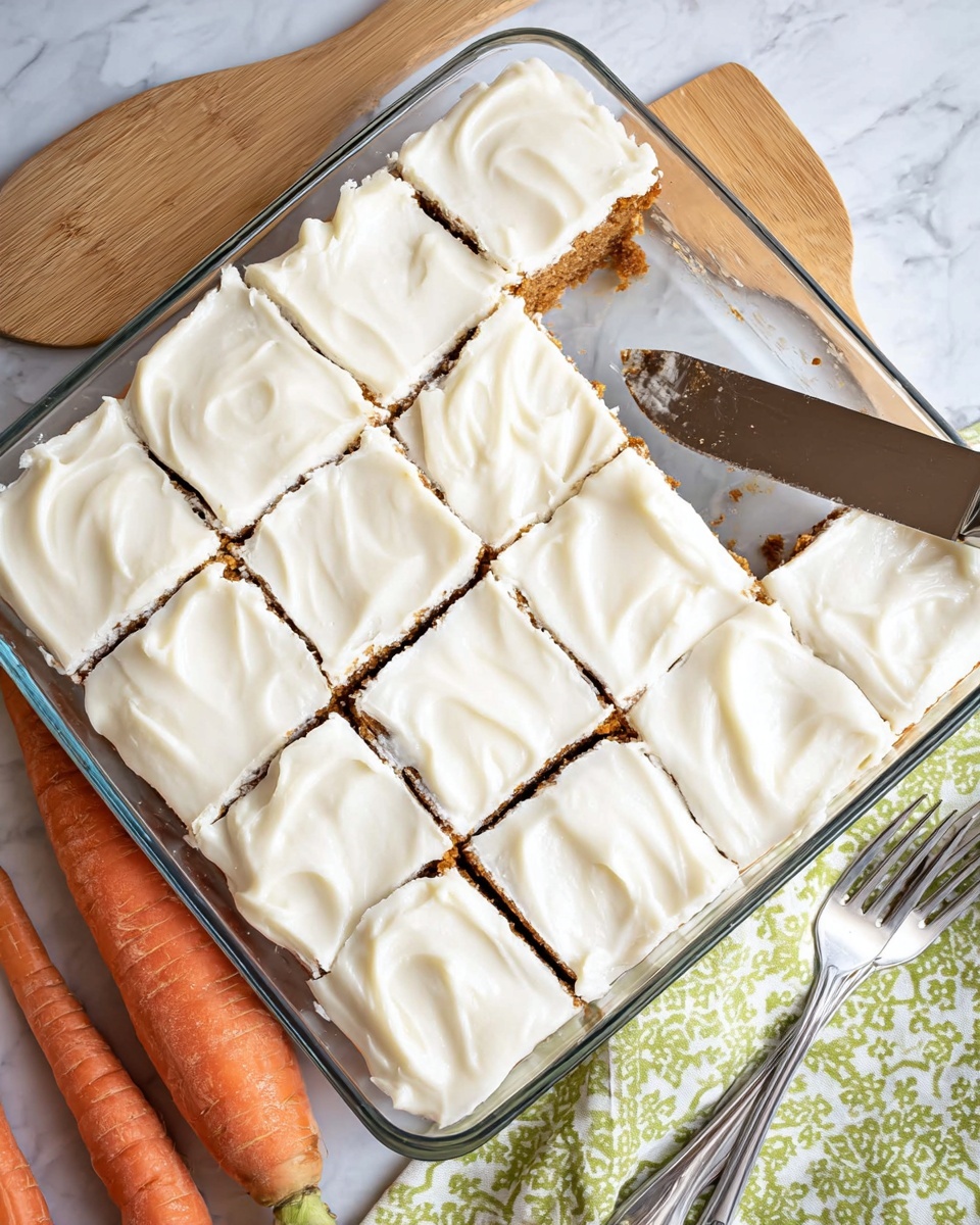 A glass baking dish filled with eighteen square pieces of cake, each topped with a thick layer of smooth white frosting showing soft, swirled texture, covering a dense brown cake base visible slightly near the edges; a large knife rests on the right side of the dish, partially cutting one piece, while a wooden spatula lies diagonally above the dish; in the lower left corner, two whole orange carrots are placed on a white marbled surface, and a silver fork along with a green and white patterned cloth napkin sit near the bottom right corner, photo taken with an iphone --ar 4:5 --v 7