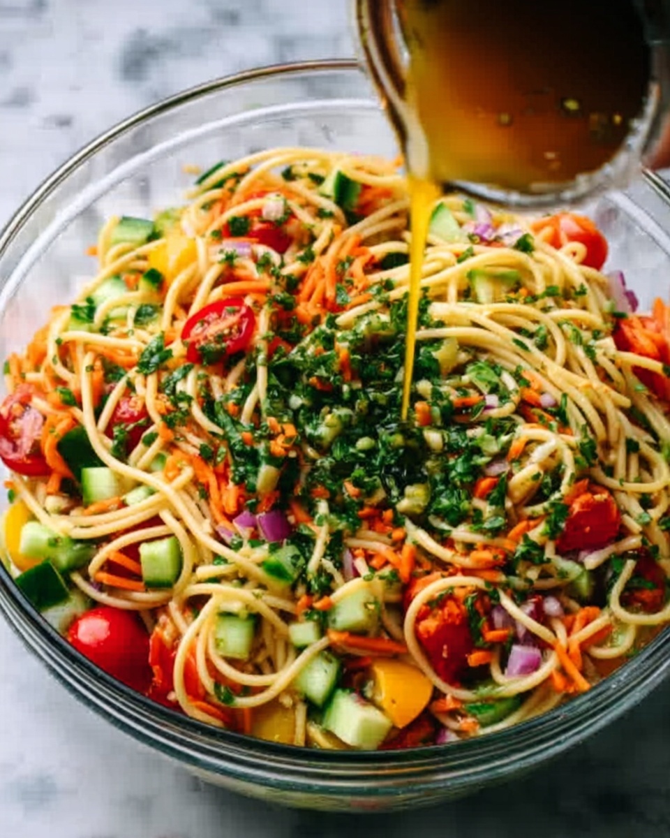 A clear glass bowl filled with a colorful noodle salad sits on a white marbled surface. The salad has four main layers: long yellow noodles tangled at the bottom, bright red cherry tomatoes and small orange carrot pieces mixed throughout, chunks of green cucumber and yellow bell pepper scattered on top, and finely chopped green herbs spread evenly over all. A woman's hand is pouring a thin golden dressing over the salad from above, capturing a sense of freshness and motion. photo taken with an iphone --ar 4:5 --v 7