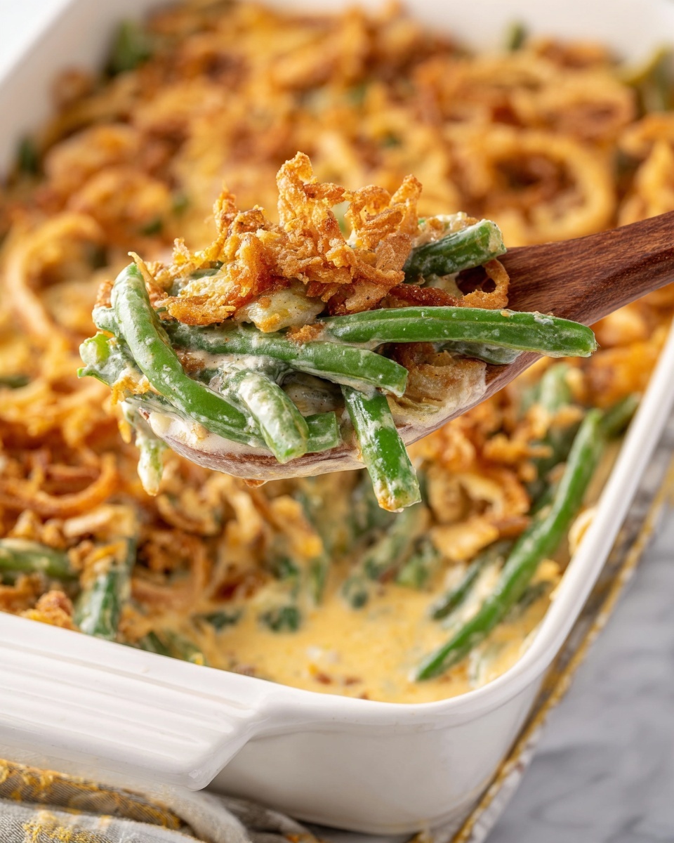 A close-up shows a white ceramic baking dish filled with a green bean casserole. The casserole has layers starting with bright green beans mixed in a creamy beige sauce, topped with crispy golden-brown fried onions scattered across the surface. A wooden spoon lifts a portion from the dish, holding green beans coated in sauce with crunchy onion bits on top. The dish sits on a white marbled surface, creating a clean and fresh background. Photo taken with an iphone --ar 4:5 --v 7