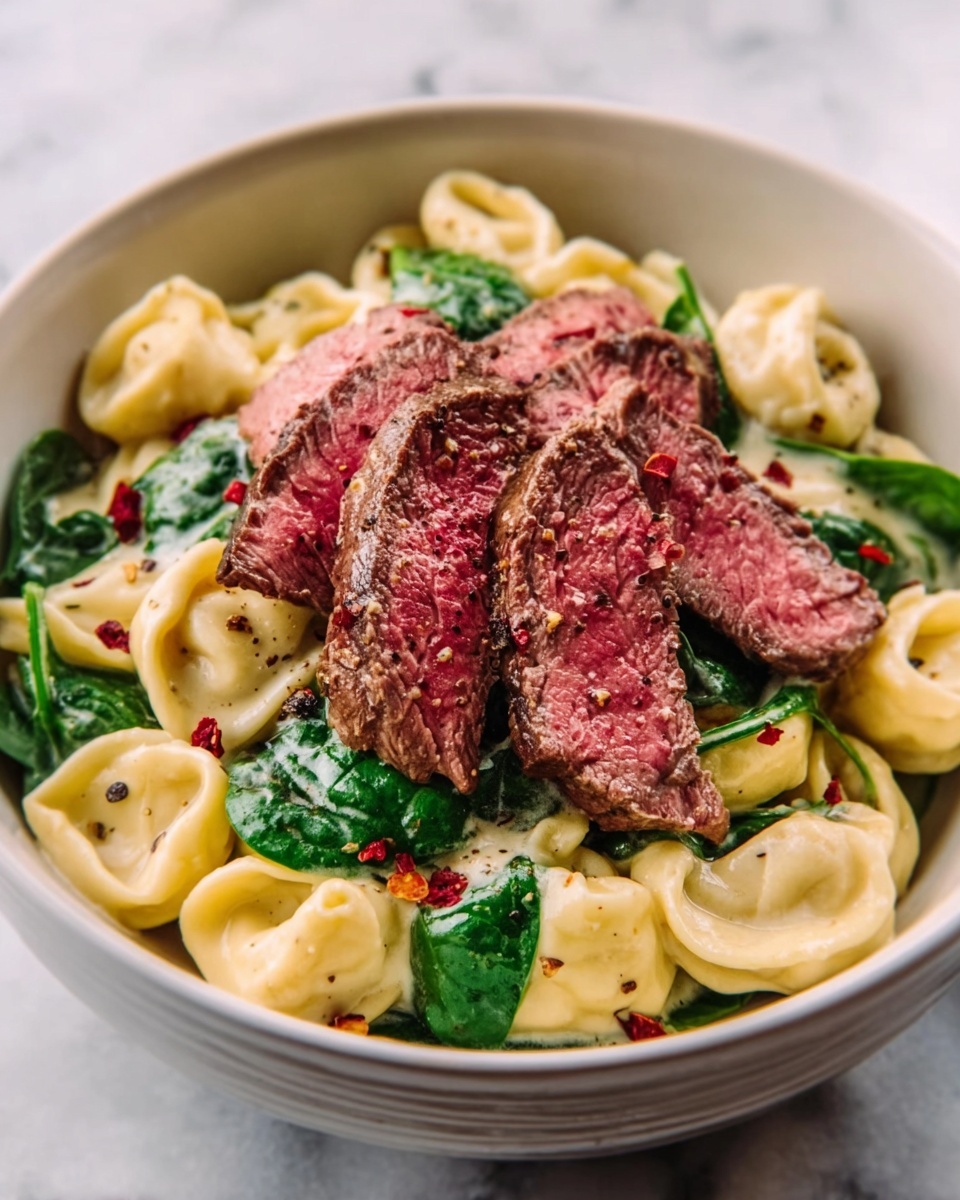 The dish shows a white bowl filled with creamy pasta tortellini that is pale yellow and smooth in texture. On top, there are several slices of medium-rare steak with a pink center and browned edges, arranged in the middle. Fresh green spinach leaves are mixed with the pasta, adding a bright green color and leafy texture. Small red pepper flakes are sprinkled over the steak and pasta, adding a touch of color contrast. The background surface is white marble, and a woman's hand holds the side of the bowl. photo taken with an iphone --ar 4:5 --v 7