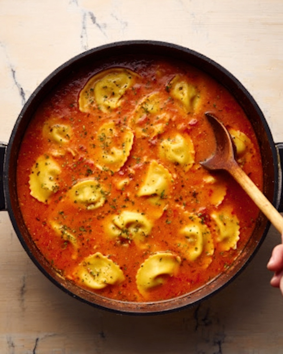 A round black pot filled with a warm red-orange soup that has smooth texture with small bits of herbs and spices floating in it. Inside the soup, visible large pieces of yellow ravioli-like pasta that have slight folds and a soft texture, floating mostly on the surface. A wooden spoon with a smooth surface is partially dipped inside the pot, with a woman's hand gently holding its handle from the right side. The pot is placed on a white marbled surface. Photo taken with an iphone --ar 4:5 --v 7