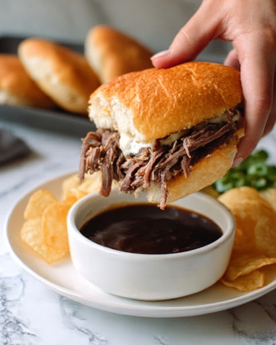 A woman's hand is holding a sandwich with a soft, golden brown bun filled with shredded roasted meat that looks juicy and tender. The sandwich is being dipped into a white bowl filled with dark brown sauce. The bowl sits on a white plate with a few potato chips on the side. The background has a white marbled texture. Photo taken with an iphone --ar 4:5 --v 7