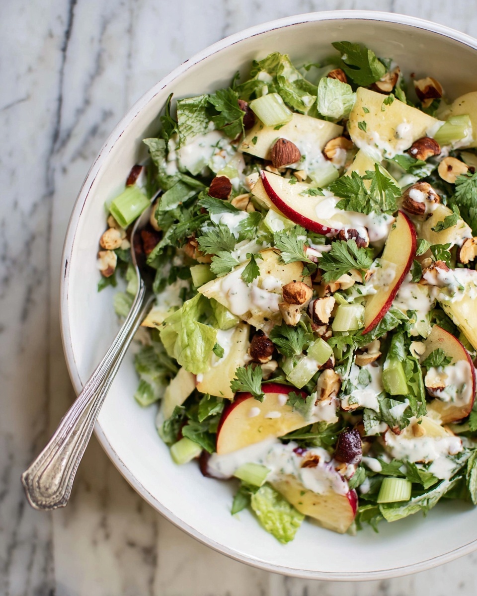A white bowl filled with a fresh salad. The bottom layer is made of crisp light green leafy greens and celery pieces. On top, there are thin slices of red and yellow apples with their skin still on, mixed with whole and chopped brown hazelnuts. The salad is sprinkled with fresh chopped parsley. A creamy white dressing is drizzled unevenly over the salad. A silver spoon is placed inside the bowl on the left side. The bowl sits on a white marbled surface. Photo taken with an iphone --ar 4:5 --v 7