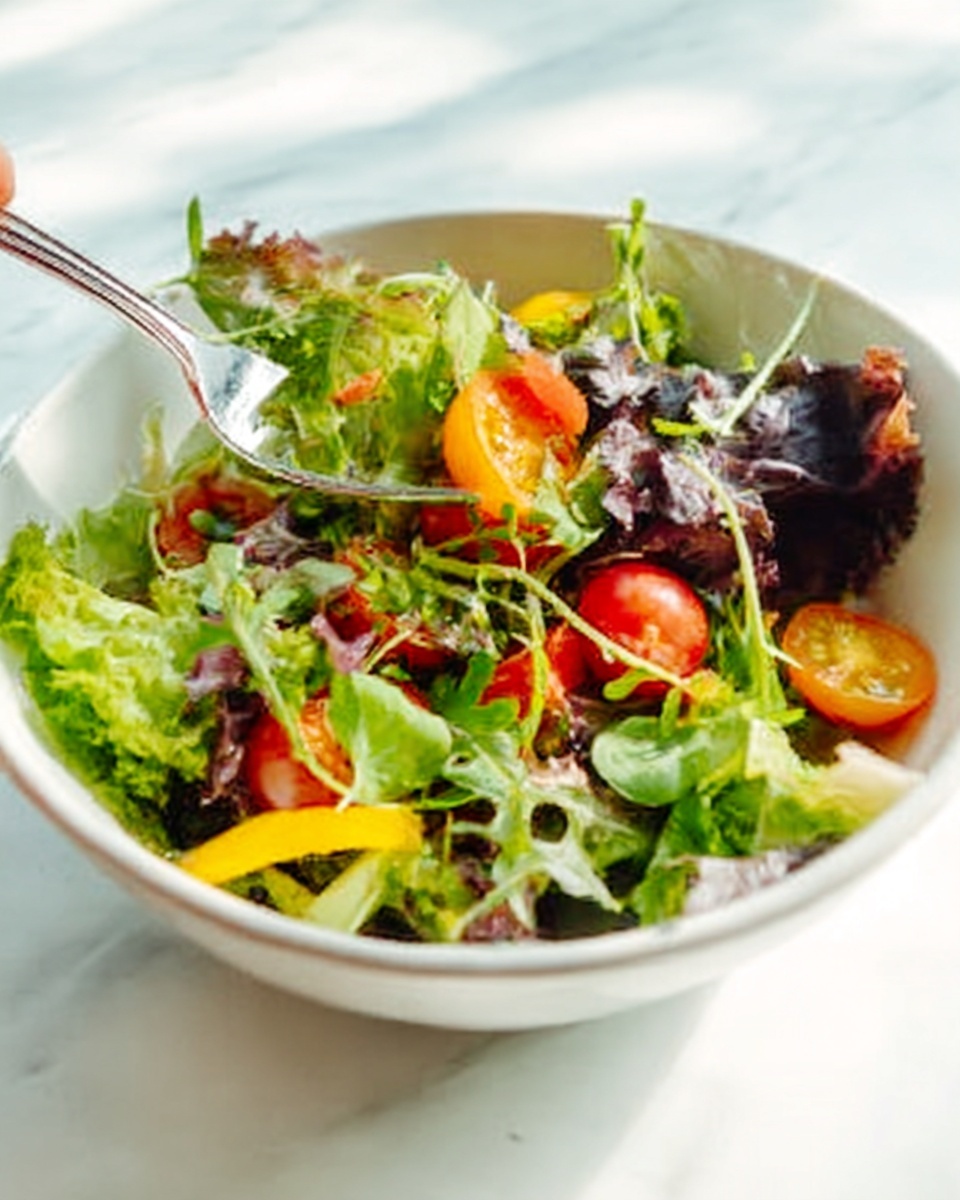 A white bowl filled with fresh mixed salad showing multiple layers: at the base, bright green and purple lettuce leaves with rough and smooth textures cover the bottom; on top, halved small cherry tomatoes with shiny red and yellow skins add color contrast; scattered lightly across are small green arugula leaves with delicate thin stems; some thinly sliced yellow bell pepper pieces add brightness; a woman's hand is reaching from the left side holding a silver fork about to take a bite; the bowl is placed on a white marbled surface with soft natural light coming from the left side, creating gentle shadows. photo taken with an iphone --ar 4:5 --v 7