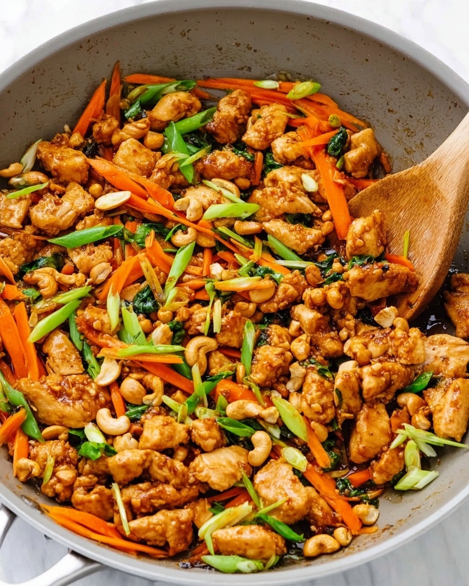 This image shows a close-up of a cooked chicken stir-fry in a light gray pan with a wooden spoon resting inside. The dish has three main layers: browned chicken pieces scattered throughout, thin orange carrot sticks spread evenly, and bright green chopped scallions sprinkled on top. There are also light tan cashew nuts mixed in with the chicken and vegetables. The chicken looks crispy and coated with a shiny sauce, while the carrots and scallions add fresh color. The pan and food sit on a white marbled surface. Photo taken with an iphone --ar 4:5 --v 7