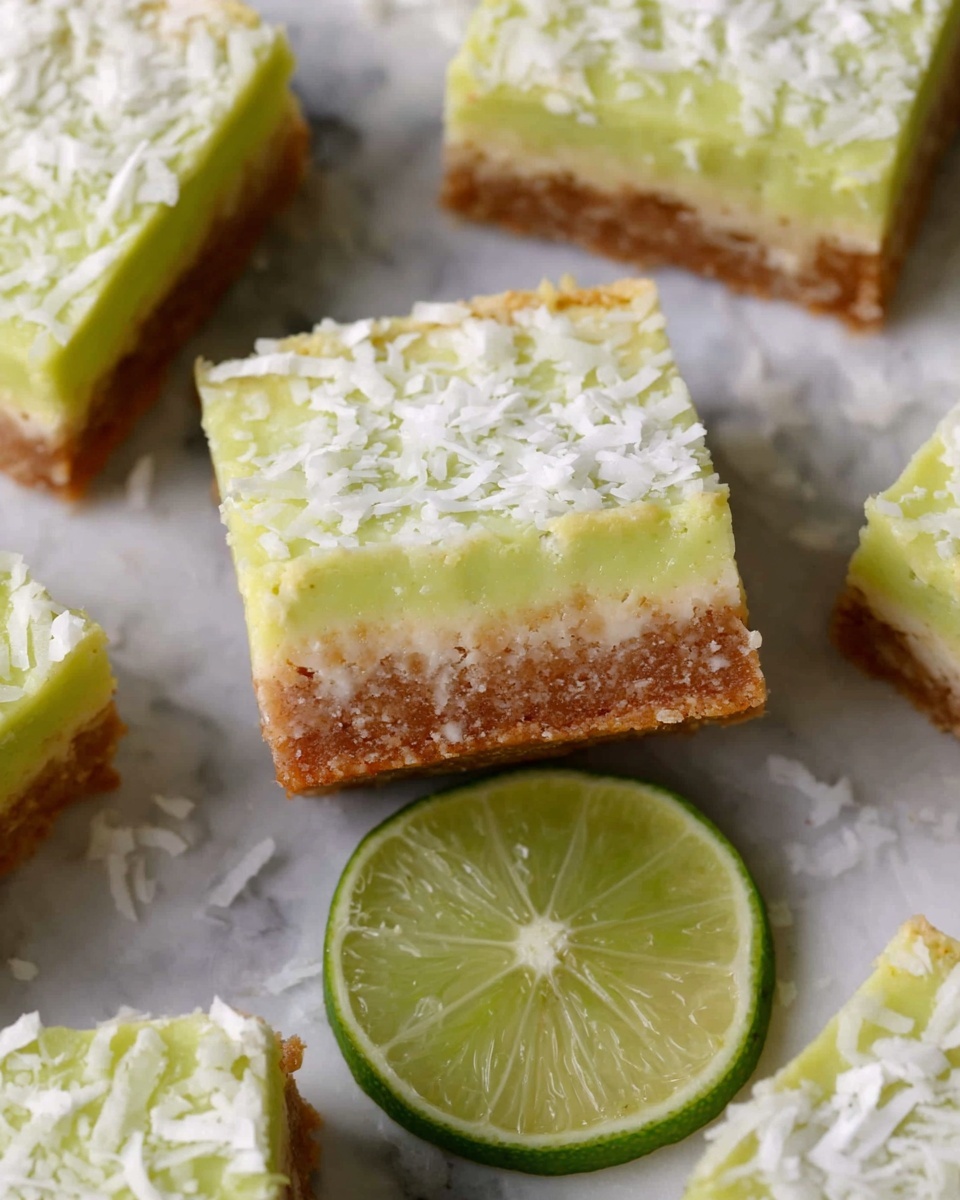 The image shows several square bars arranged on a white marbled surface. Each bar has two layers: the bottom layer is thick, crumbly, and brown with visible small chunks, giving a textured look, while the top layer is a smooth, pale yellow-green color, spread evenly, with shredded white coconut sprinkled on top. A halved lime with bright green color and visible segments is placed among the bars, adding a fresh touch to the scene. Photo taken with an iphone --ar 4:5 --v 7