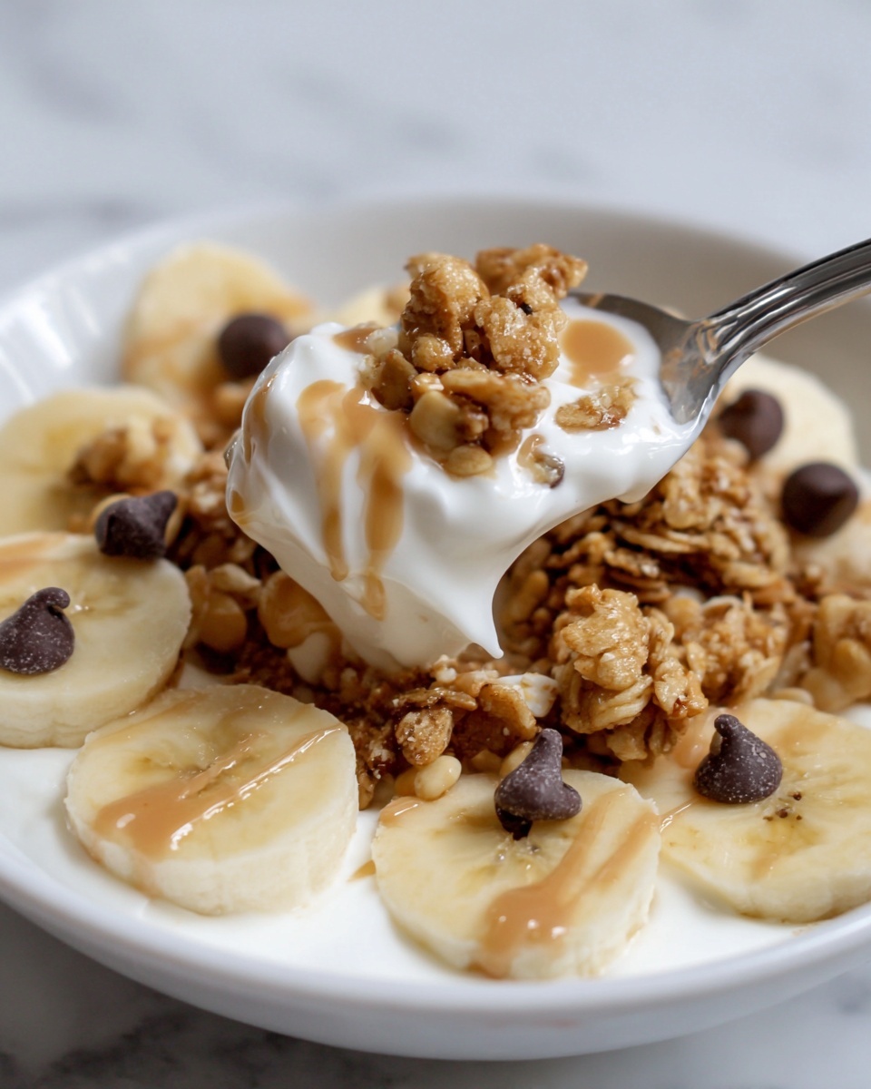 This image shows a close-up of a white bowl filled with a layered breakfast dish. At the bottom, there is a thick layer of creamy white yogurt. On top of the yogurt, there are evenly spread round slices of pale yellow banana. Above the banana slices, there are clusters of golden-brown granola with visible oats and small round nuts. Scattered on and around the granola are a few dark chocolate chips. A light brown sauce is drizzled over the top, adding a shiny texture contrast. A silver spoon is lifting a bite of the dish from the right side of the bowl. The bowl is placed on a white marbled surface. Photo taken with an iphone --ar 4:5 --v 7