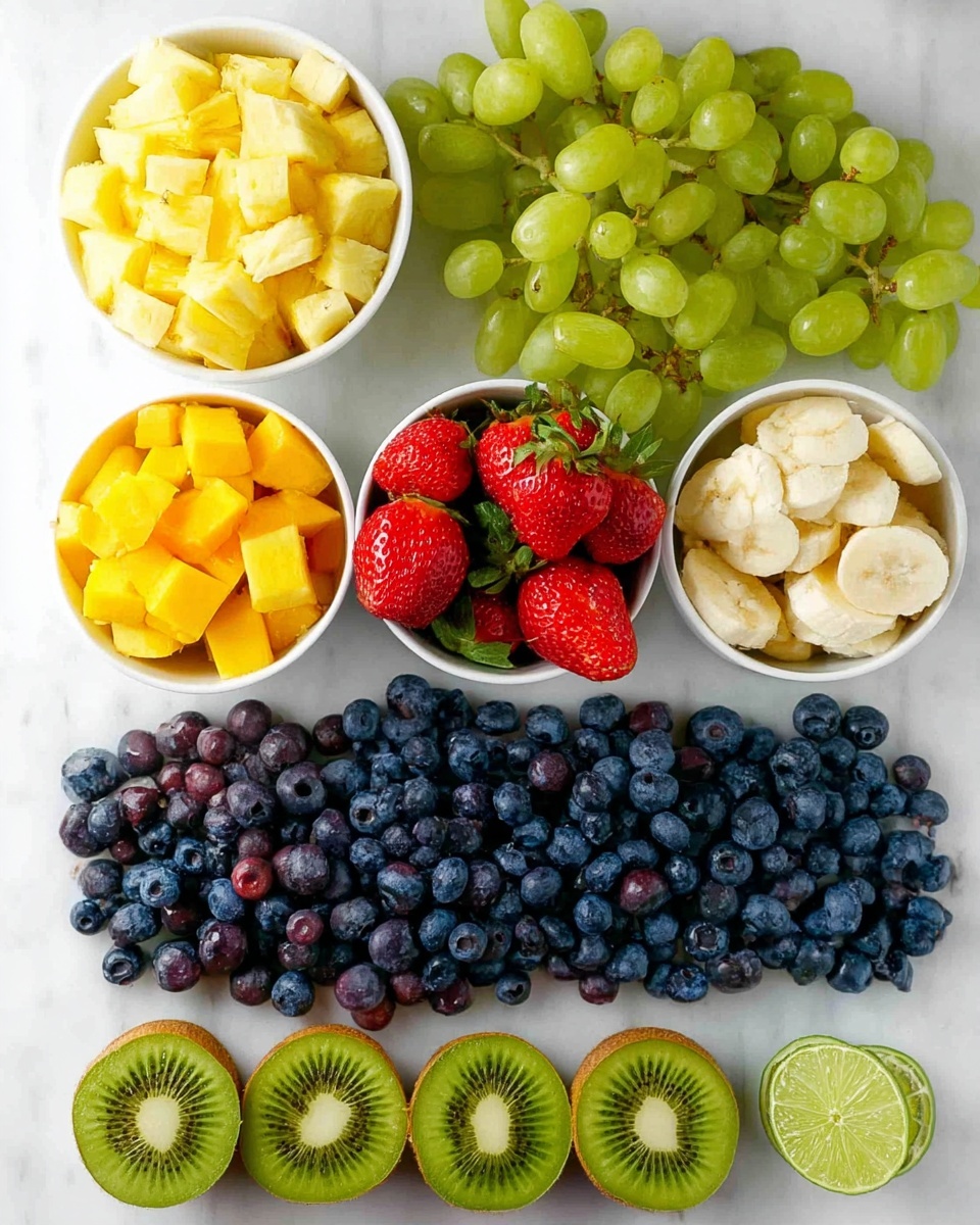 A top view of a flat arrangement of fresh fruit on a white marbled surface. At the top, there is a white bowl filled with small pieces of pineapple and next to it a bunch of green grapes. Below this, there is another white bowl filled with small pieces of mango and banana slices on one side. Nearby, there is a group of red strawberries with green leaves. Along the bottom, six halved kiwis are lined up side by side showing their green inside and black seeds. At the very bottom, a large row of blueberries stretches across the image. In between the bowls and fruit, two lime halves are placed on the surface. Photo taken with an iphone --ar 4:5 --v 7