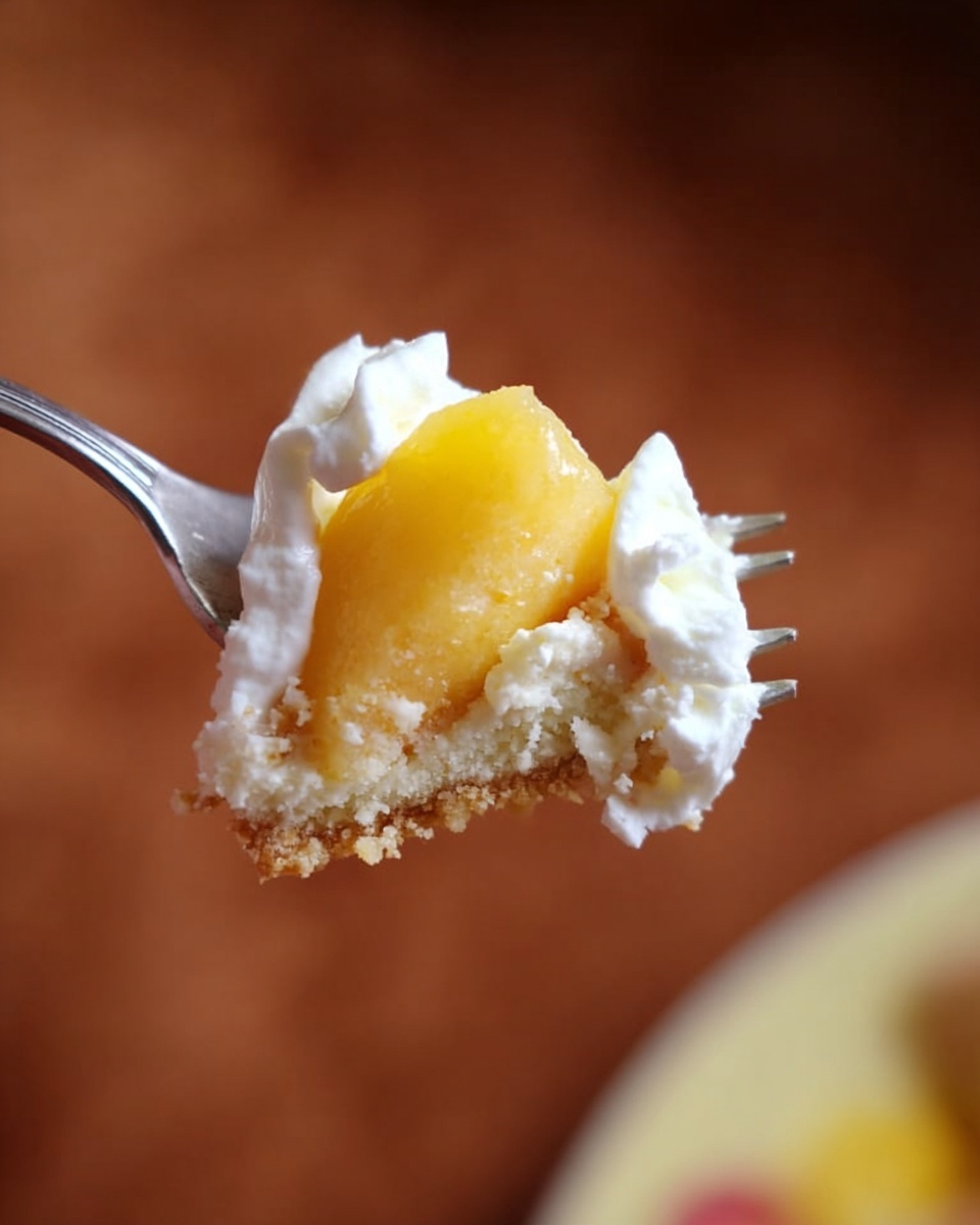 Peach Custard Pie with Greek Yogurt and Streusel Topping Recipe 5 A close-up of a silver fork holding a small piece of soft yellow fruit, likely peach or mango, topped with a thick dollop of white cream and crumbs of a pale beige cake or crust, against a blurred warm brown background with hints of red and yellow. Photo taken with an iphone --ar 4:5 --v 7