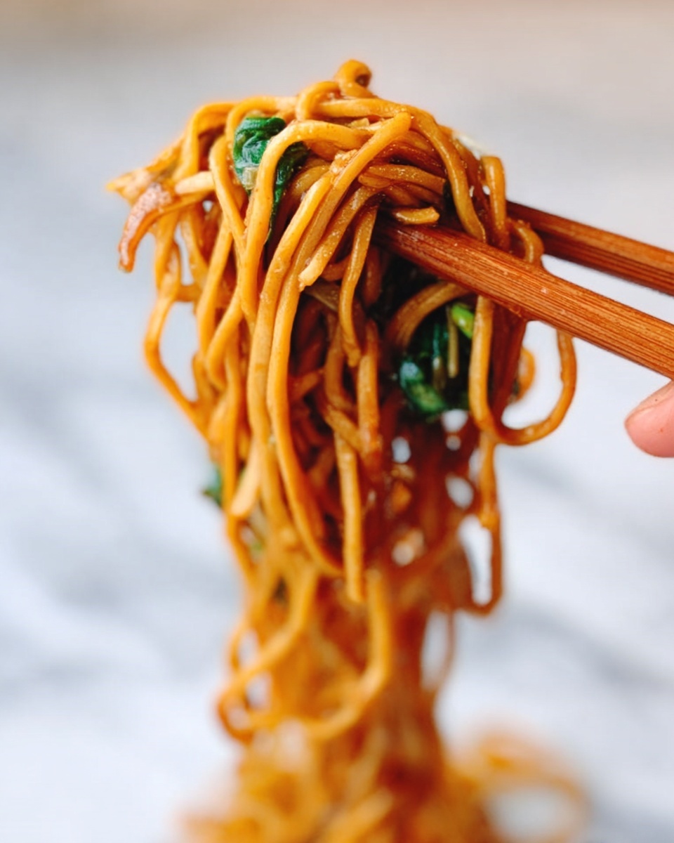 A close-up of thick noodles wrapped around a wooden chopstick held by a woman's hand. The noodles are light brown in color, coated with a shiny sauce, and mixed with some green leafy vegetables that add a fresh touch. The background is soft and blurred with a white marbled surface below. photo taken with an iphone --ar 4:5 --v 7