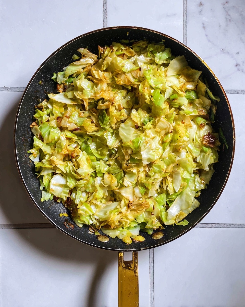 A top view of a black frying pan with a golden handle filled with cooked chopped cabbage. The cabbage has layers of light green and yellow pieces with some browned edges, showing a soft and slightly crispy texture. The pan is placed on a white marbled tiled surface. photo taken with an iphone --ar 4:5 --v 7